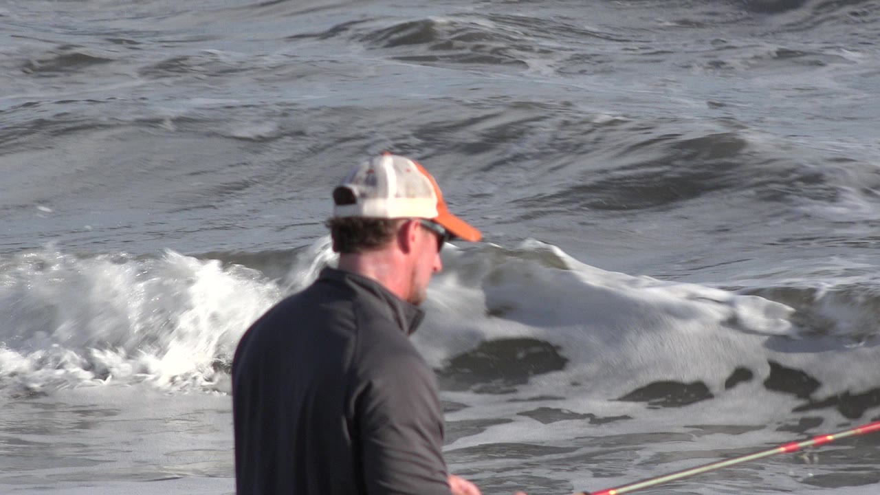 The fisherman remains near the Los Cabos waterline as white foam rolls behind his low-held fishing rod.