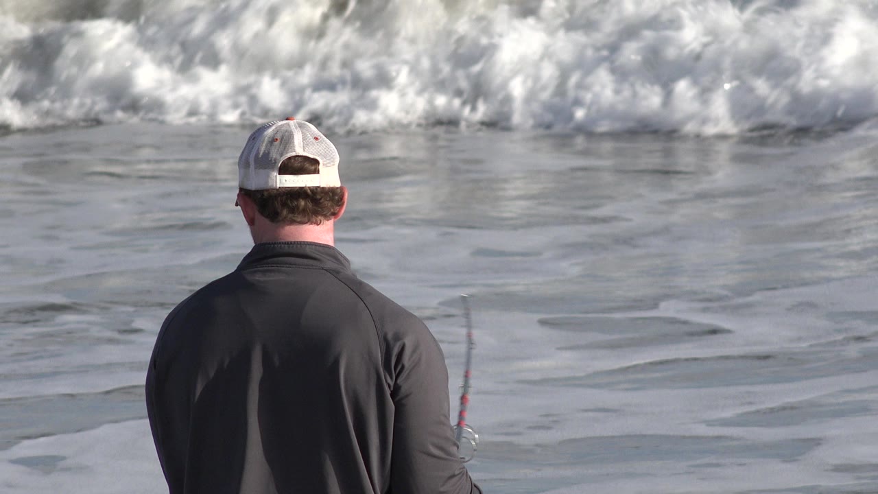 At 0:01 in Los Cabos, Mexico, the back of the fisher remains centered while the rod appears at the side and a band of foamy surf breaks farther out.