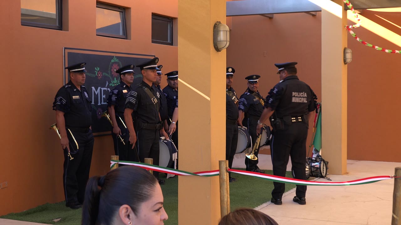 Uniformed officers stand in front of a decorated wall sign and event barrier.