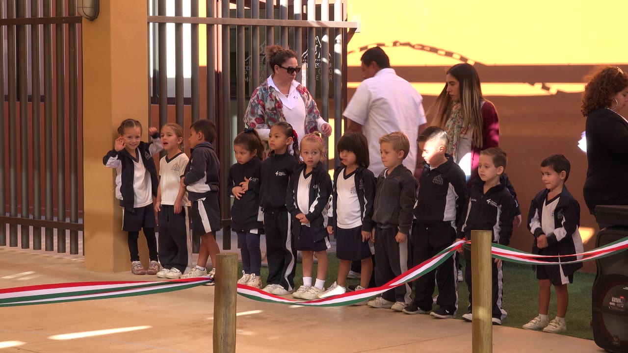 Children line up behind a tricolor ribbon with adults nearby.