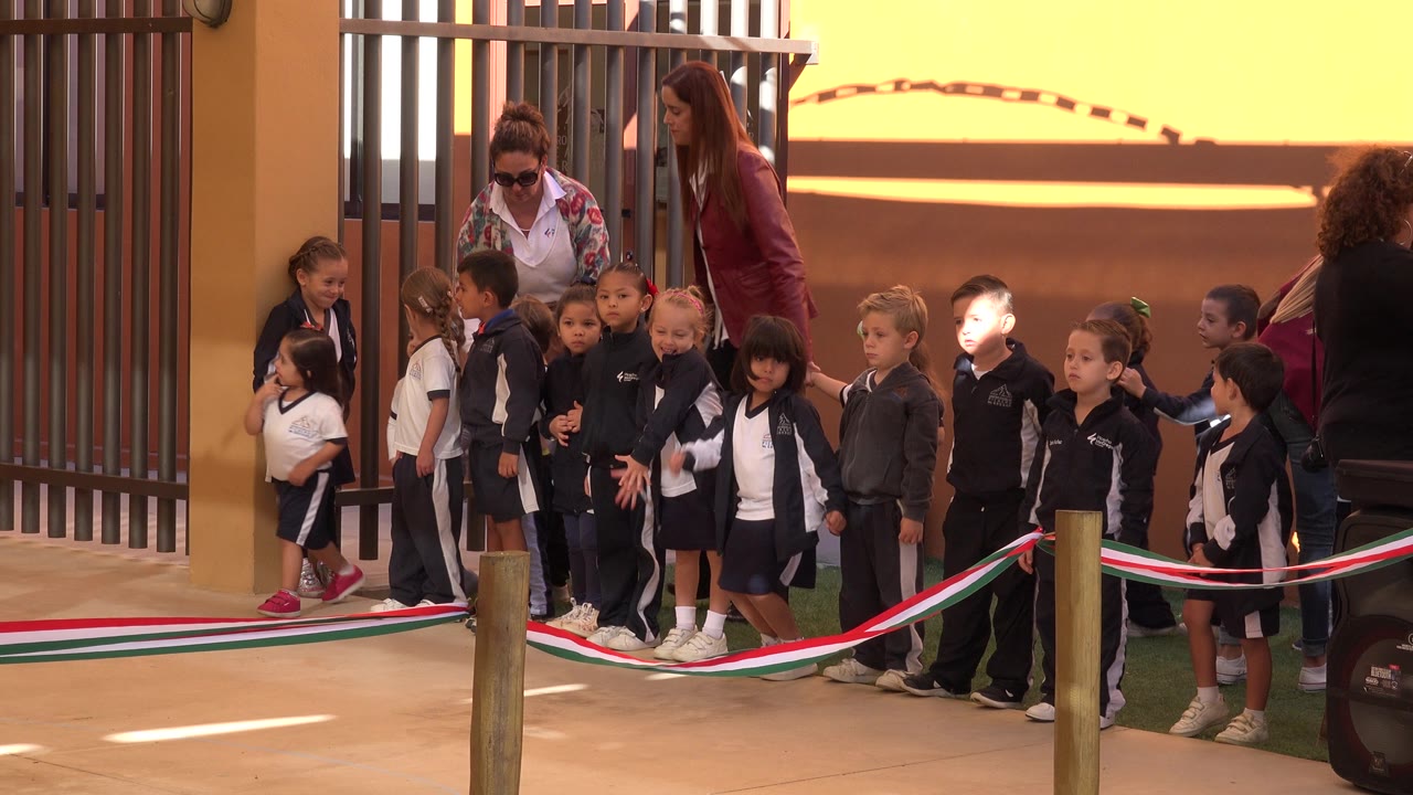 Children lined up behind rope barriers with adults nearby.