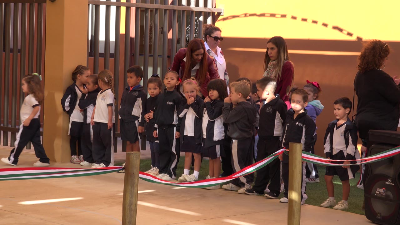 At 0:01, the children remain grouped outside in San Jose Del Cabo, Mexico, with one child walking along the left edge and adults positioned behind the line.