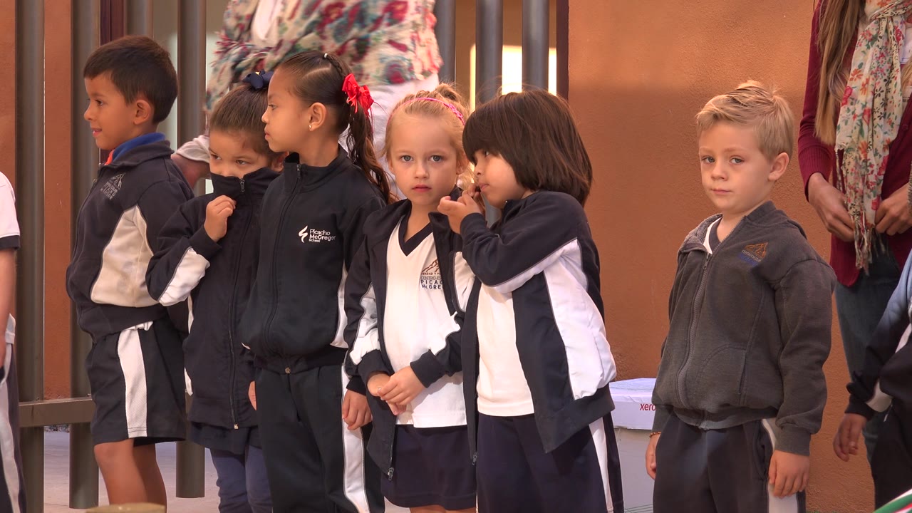 Children in school uniforms waiting beside a teacher or parent.