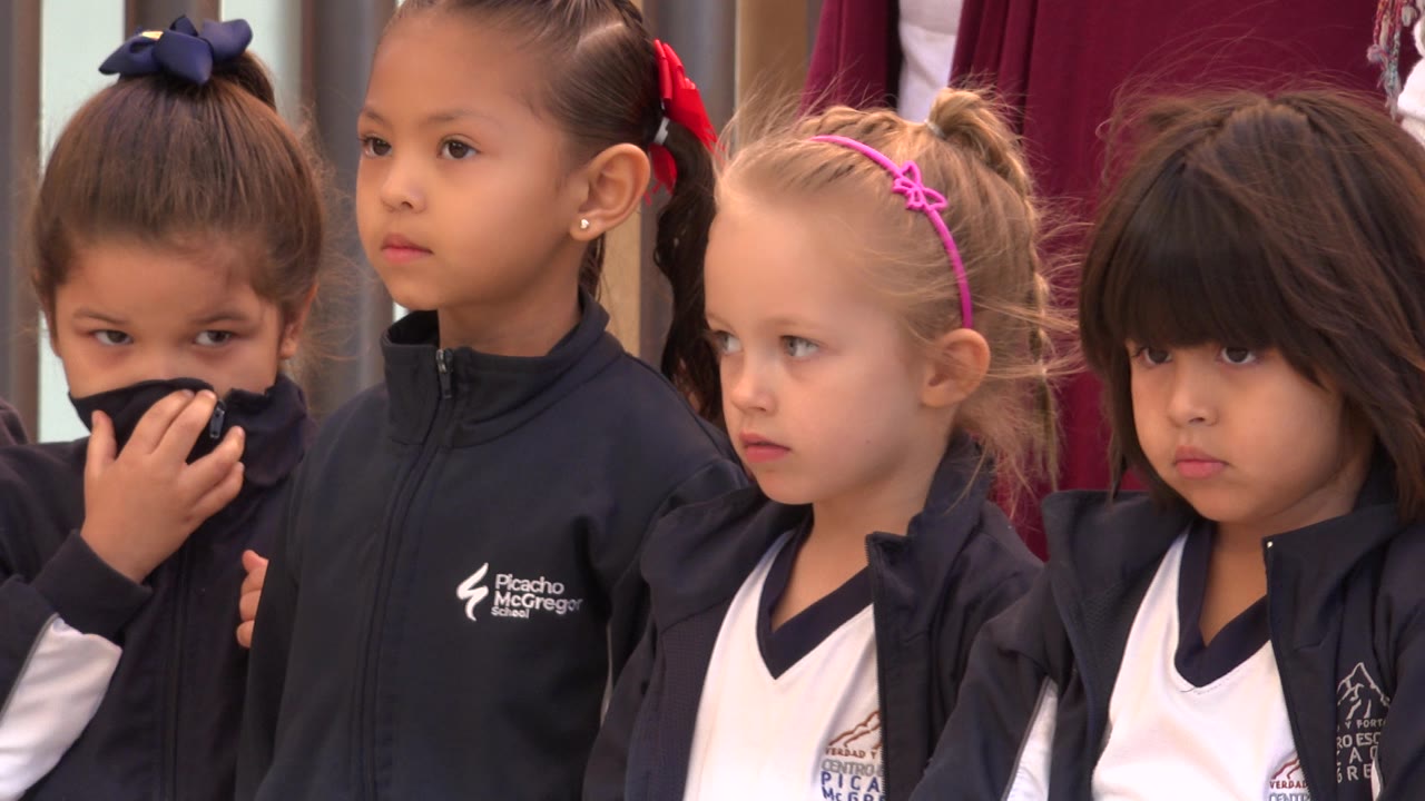 Four girls in matching dark outerwear and white shirts face the camera area in San Jose del Cabo, Mexico, while the left girl covers part of her mouth with her jacket.