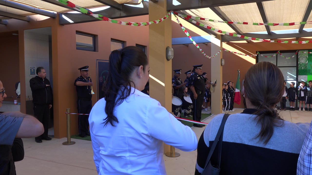 Audience members watch a uniformed band and children during an indoor ceremony.
