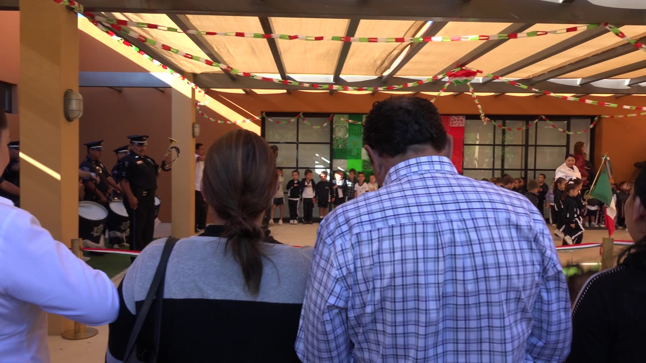 Two adults stand close to the camera while children and uniformed participants remain across the decorated courtyard in San Jose del Cabo, Mexico.