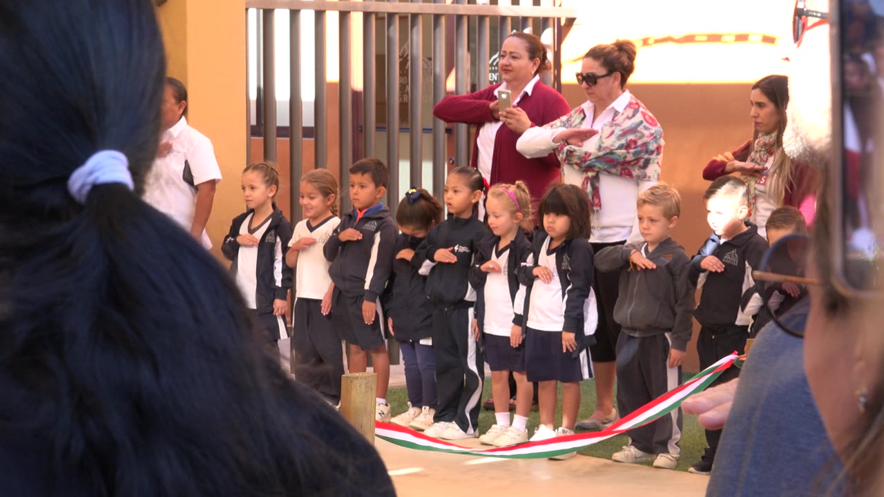 Girls in school clothing stand outdoors behind foreground spectators.
