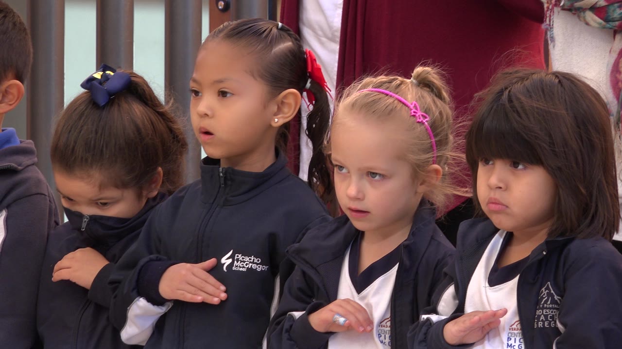 Children in navy jackets stand together with hands over hearts.