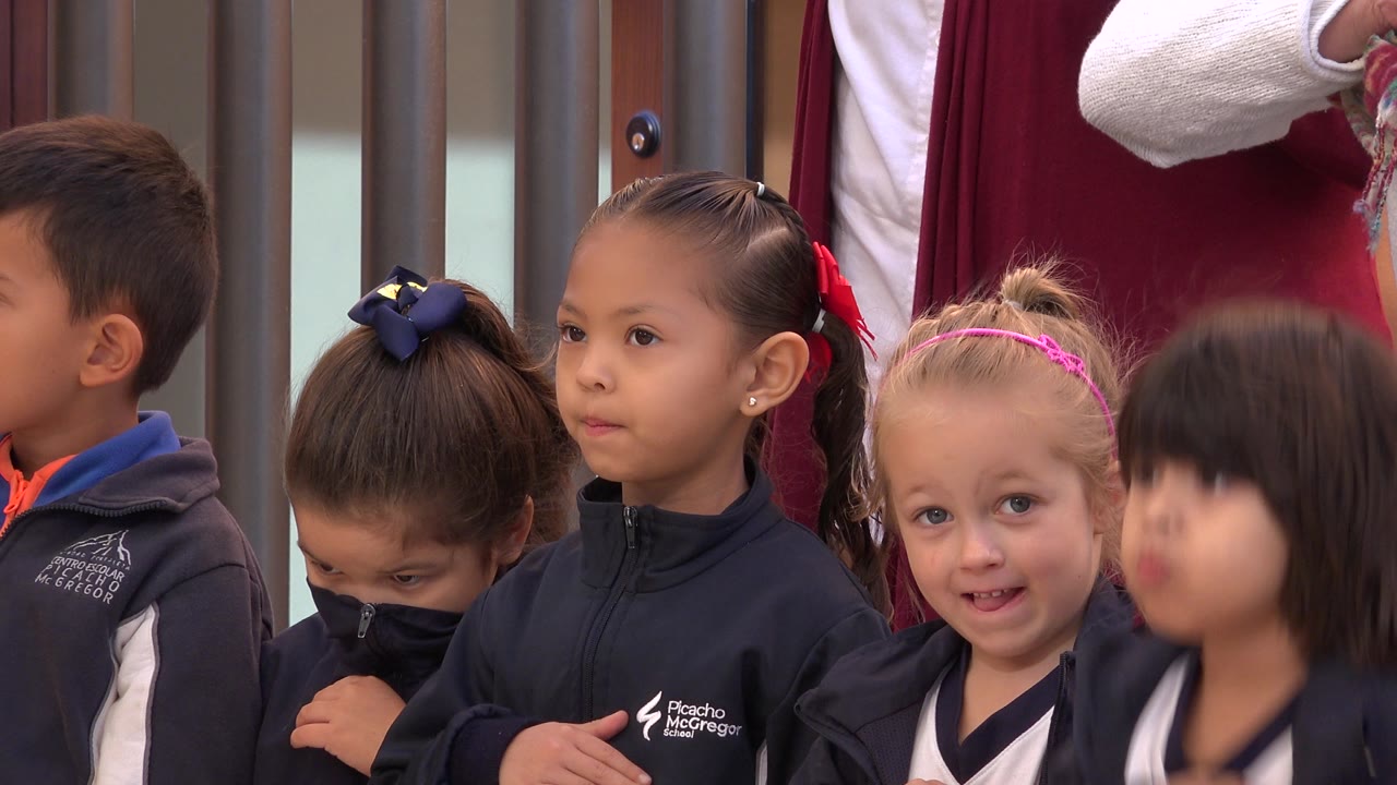 A San Jose del Cabo lineup of young children remains framed at chest height, with a girl facing forward, another child looking down, and an adult cropped behind the row.