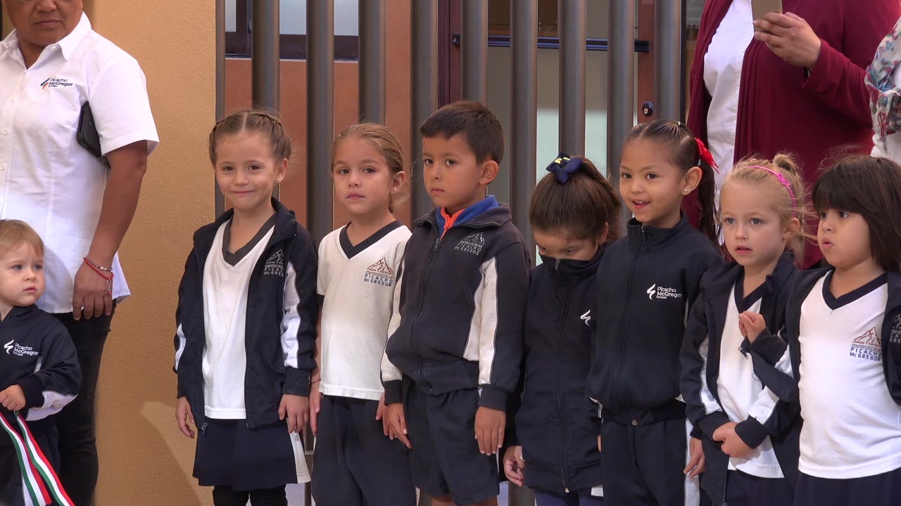 Young children lined up beside adults outside a building.