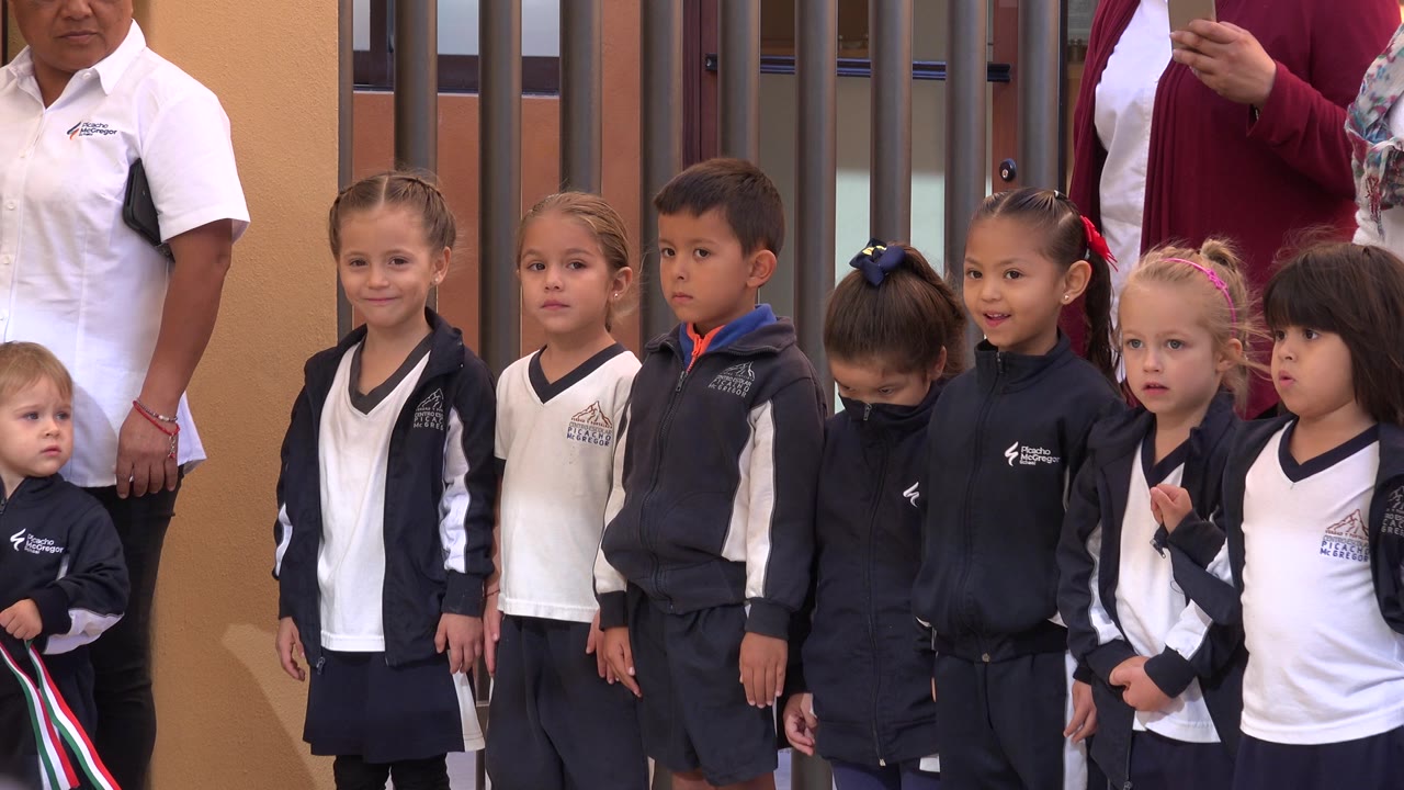 A group of children in navy and white school clothing faces forward in San Jose del Cabo, Mexico, with adults partially cropped behind them.