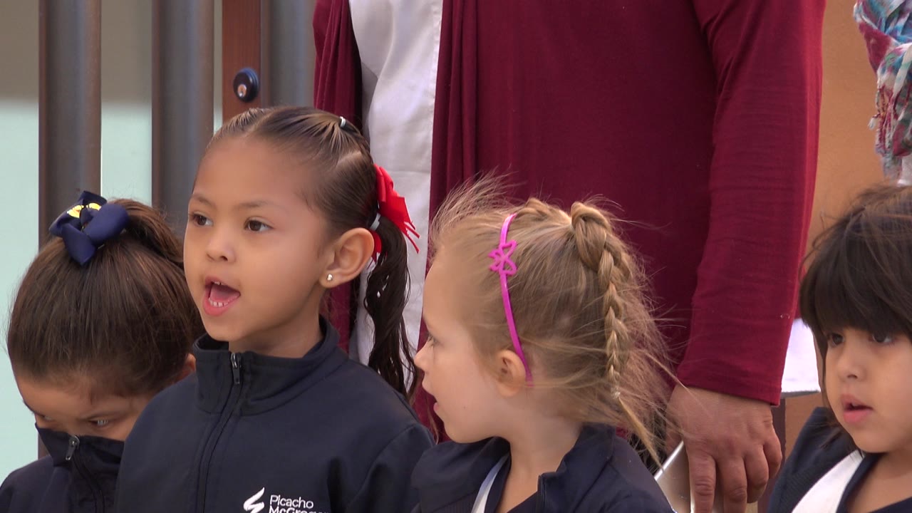 Young children in navy school uniforms stand together near adults.