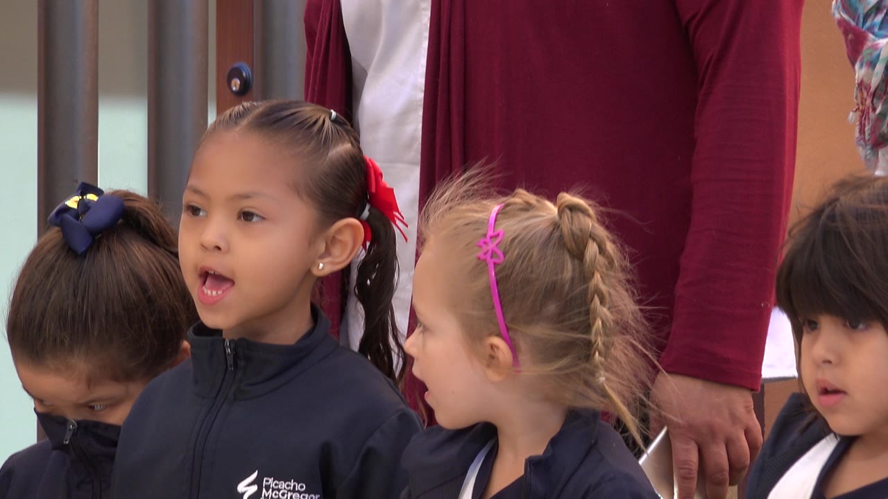 Children in San Jose del Cabo, Mexico, remain grouped in navy school jackets, with a girl in the center looking ahead and another child turned sideways beside her.
