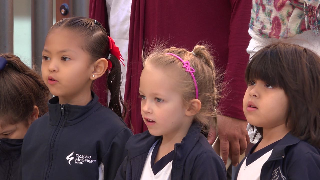 At 0:00, young girls in navy and white clothing stand close together in San Jose del Cabo, Mexico, looking toward something off-camera while adults are cropped behind them.