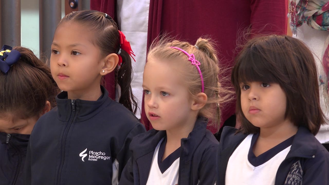 Young girls in navy school jackets and white uniform tops stand close together during a school performance in San Jose del Cabo, Mexico.