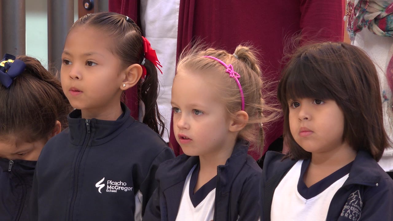 A close group view shows uniformed girls in San Jose del Cabo, Mexico, with one child wearing a pink headband and another facing forward beside her.