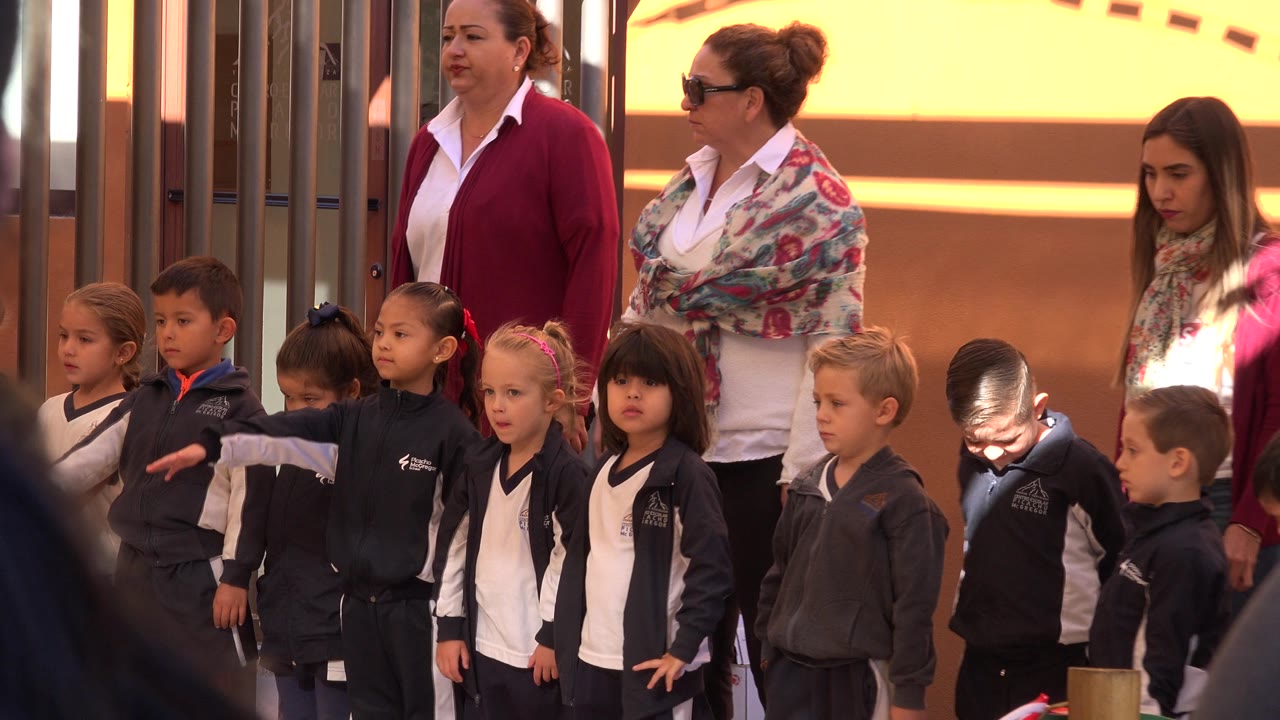 Children in uniforms stand in a row with adults behind them.
