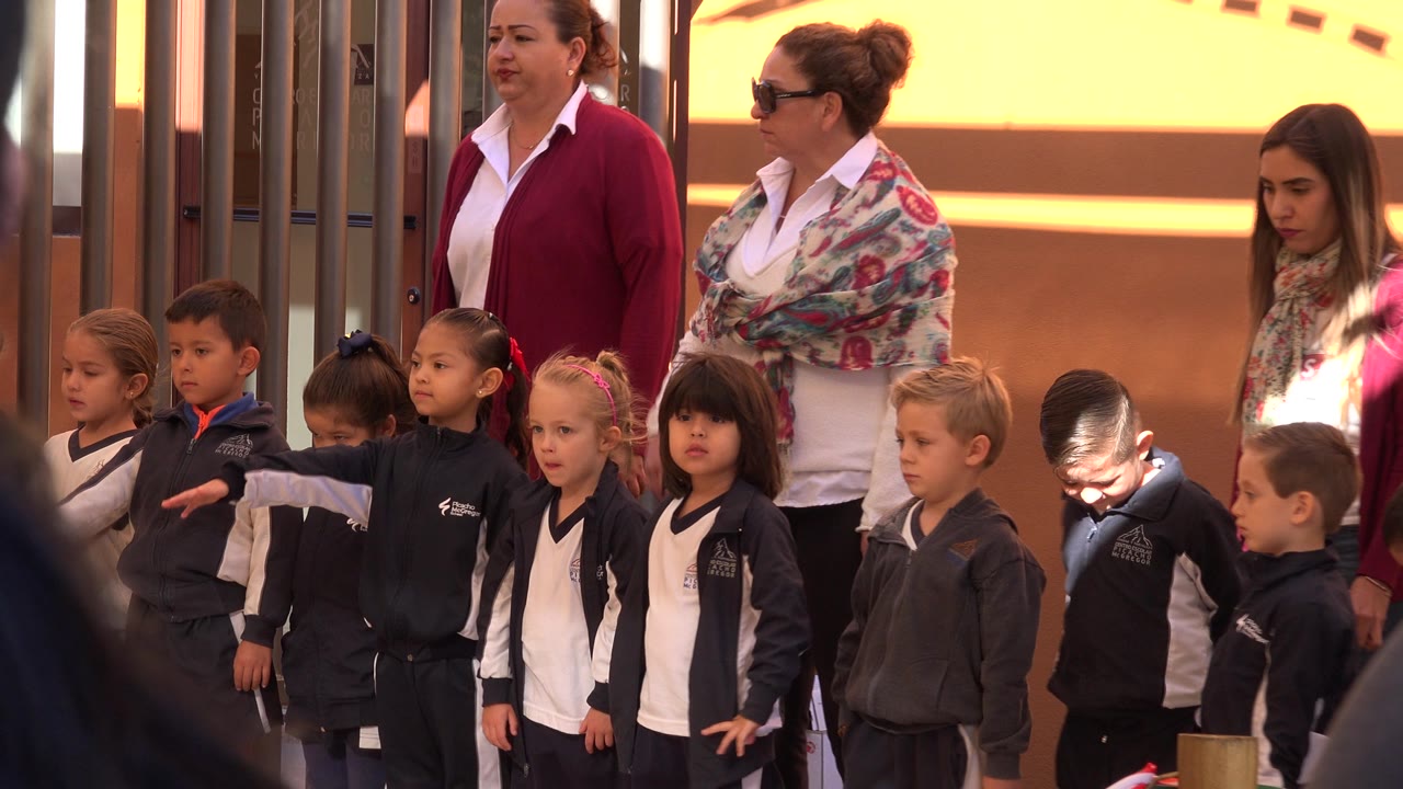 One second in, the San Jose del Cabo footage shows the same line of boys and girls in uniform with adults standing close behind them near metal railings.