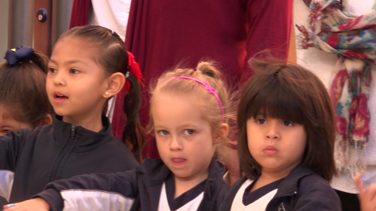 At 0:01, three young children in uniforms are framed tightly in San Jose del Cabo, Mexico, with one child looking toward the camera and adults cropped above them.