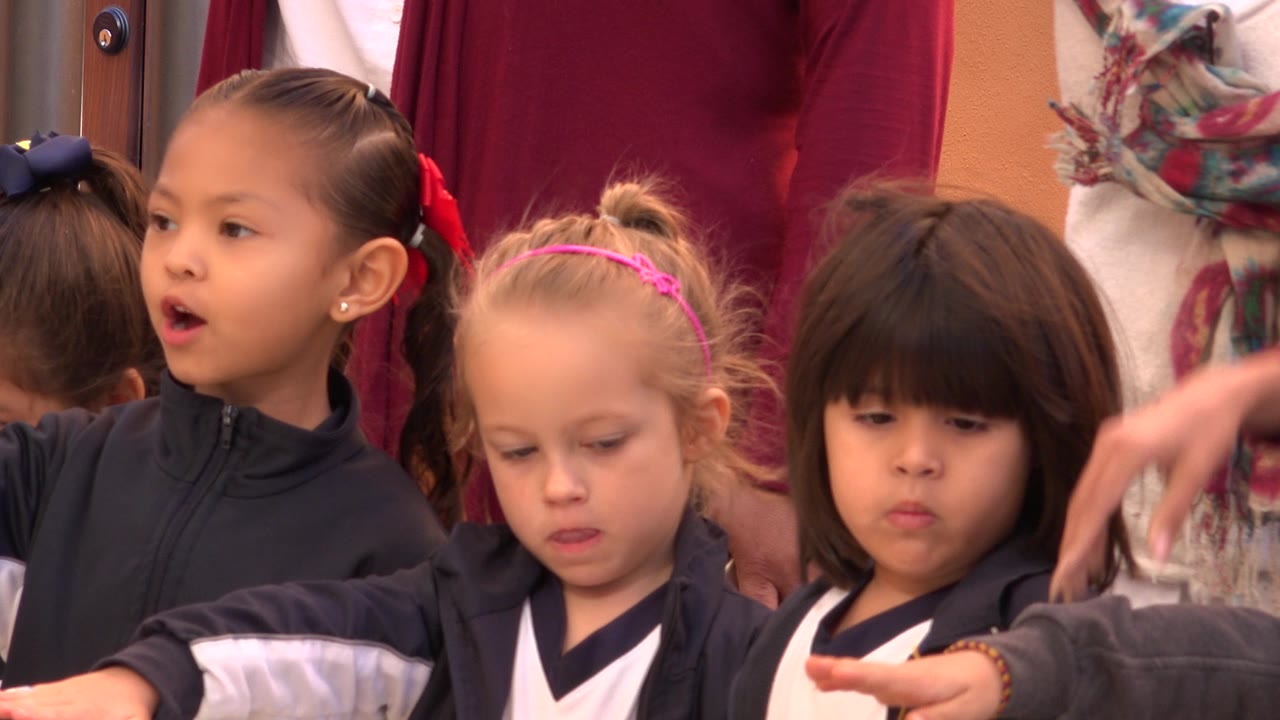 Children in uniforms stand shoulder to shoulder as one child opens her mouth.