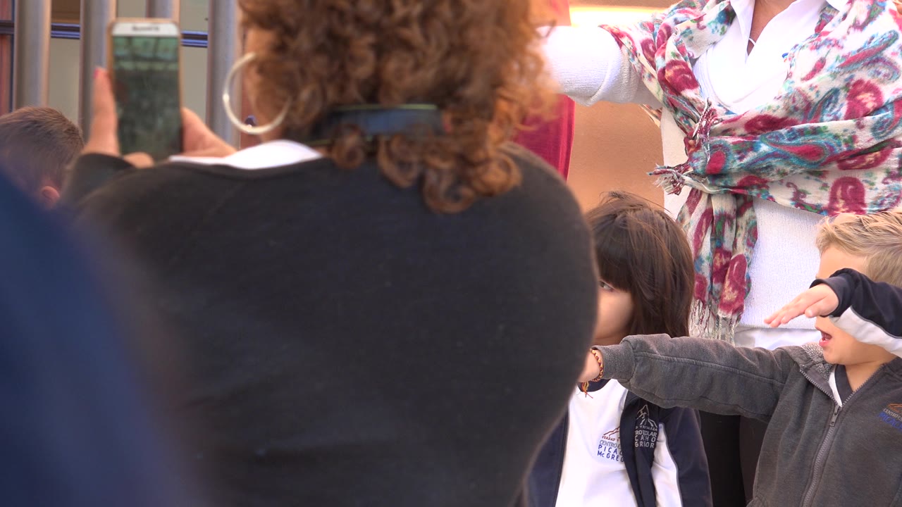 At 0:01 in San Jose del Cabo, the camera view remains partly blocked by a foreground adult as children and adults cluster near the gates and a boy keeps his arm extended.