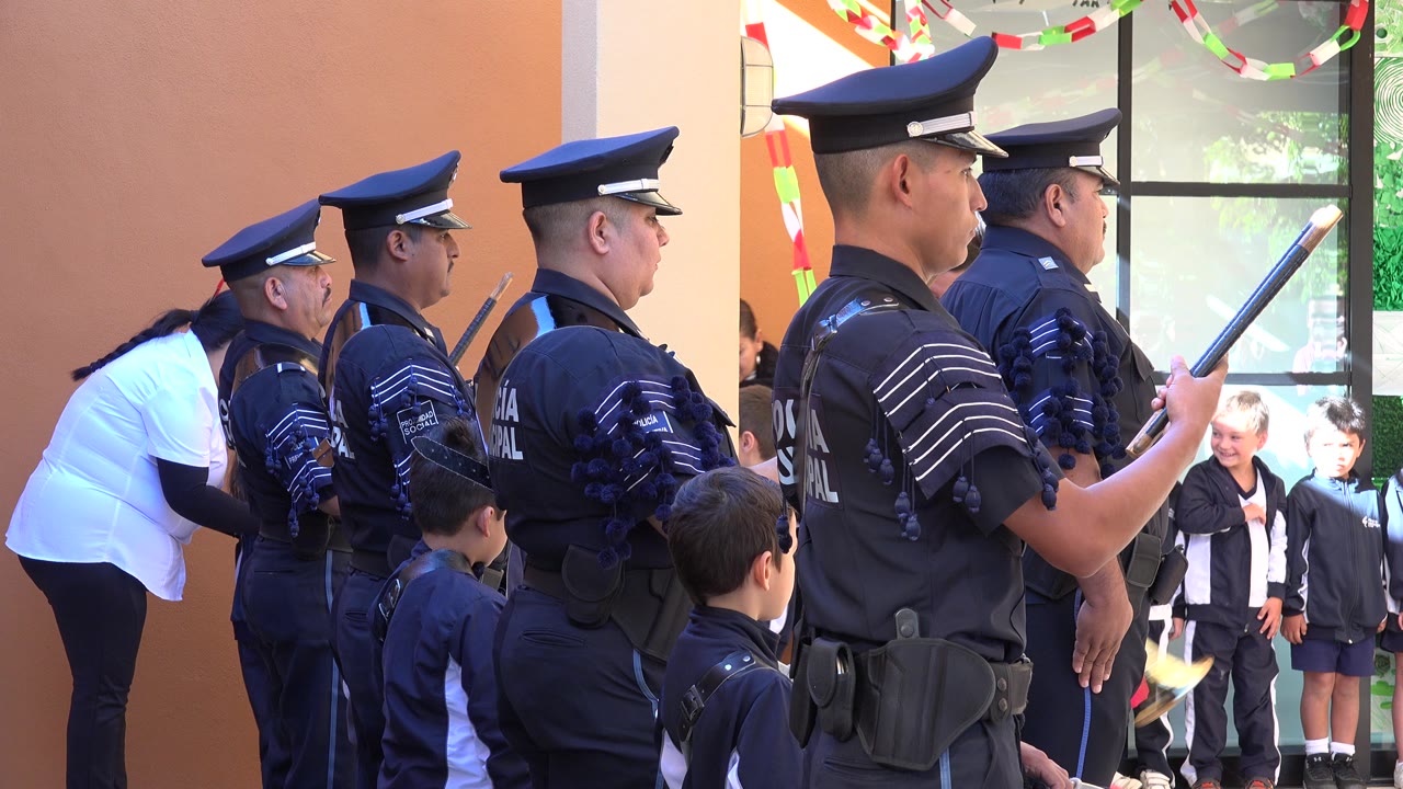 At 0:01, the police lineup remains side-on, with a child in the foreground and more children framed by the window and doorway in San Jose del Cabo.