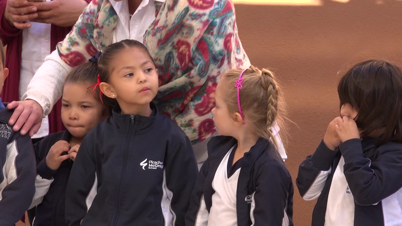 Children in matching navy and white warmups look around in San Jose del Cabo, Mexico, as adults remain partly cropped in the background.