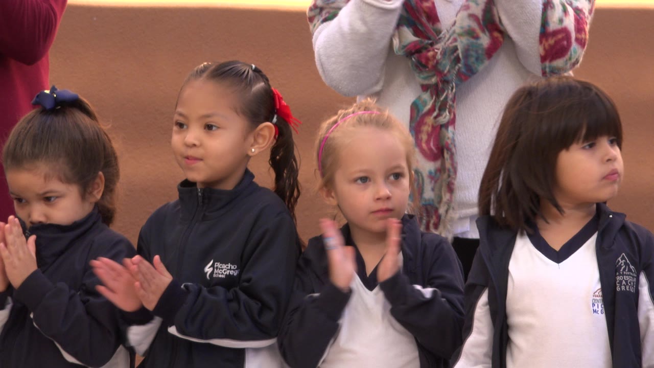 Young children in navy and white sports uniforms clap together at a recreational event in San Jose del Cabo, Mexico, with adults cropped behind them.