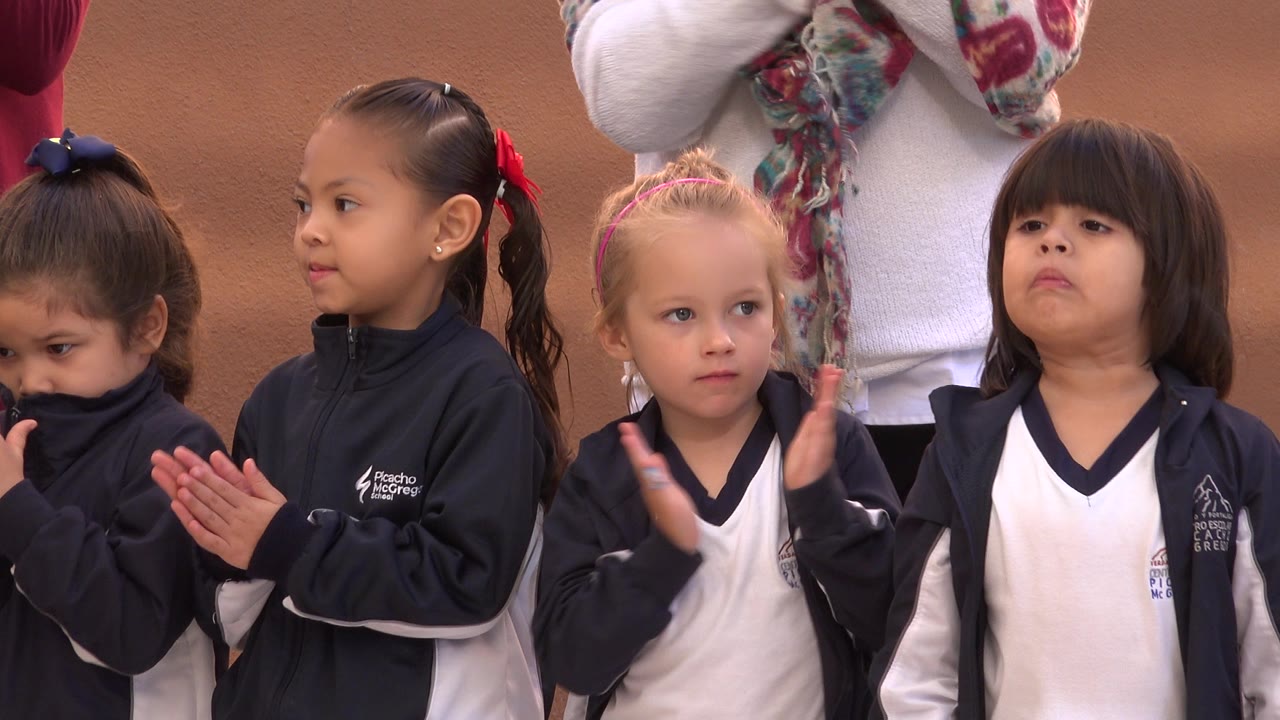 Children clapping with adults standing behind them.