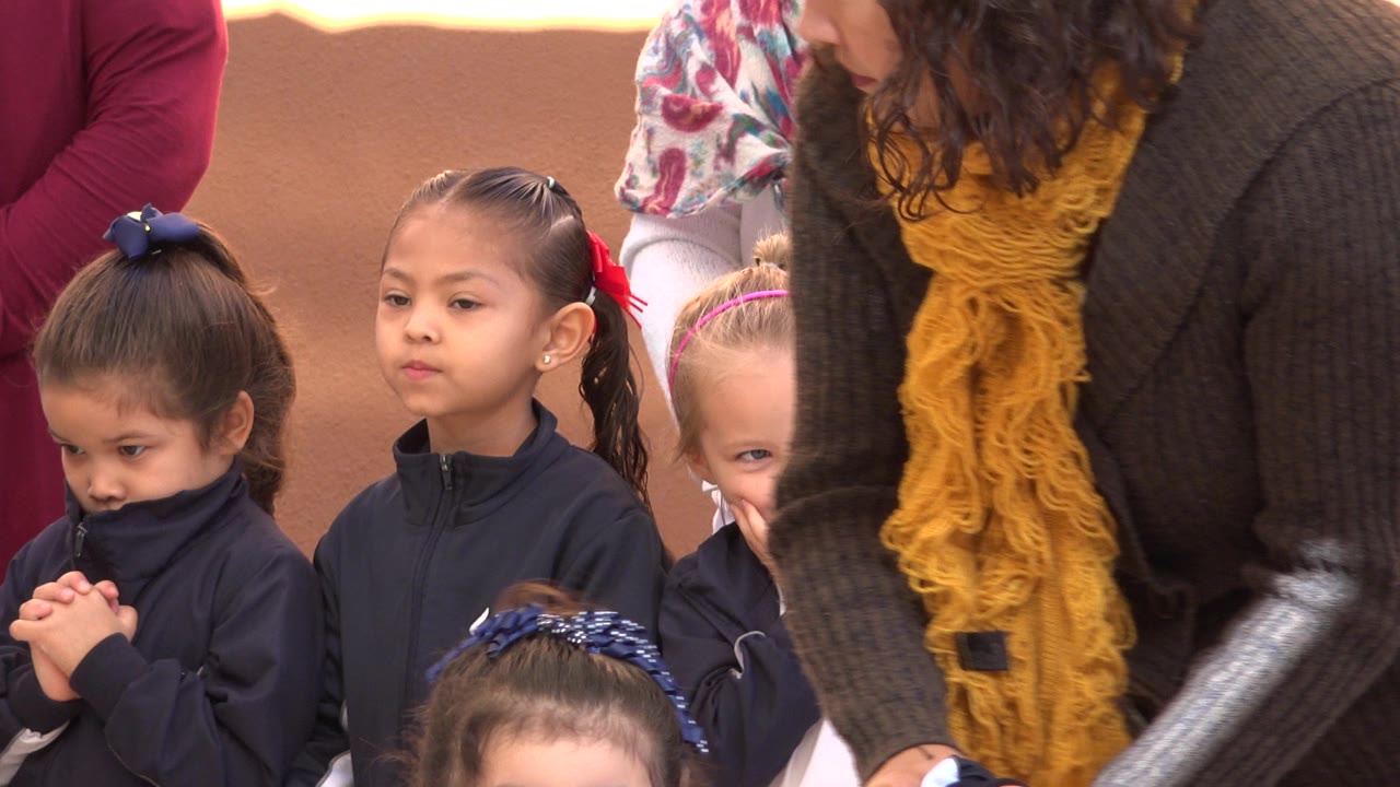 Two young girls in dark jackets stand near adults during a children’s event.