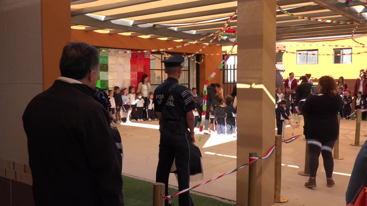 Adults and a uniformed officer watch children lined up in a pavilion.