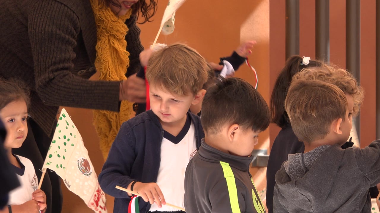 Children in uniforms hold small flags beside a teacher.