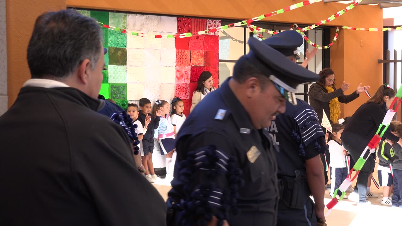 Police officer and adult watching children lined up in a courtyard.