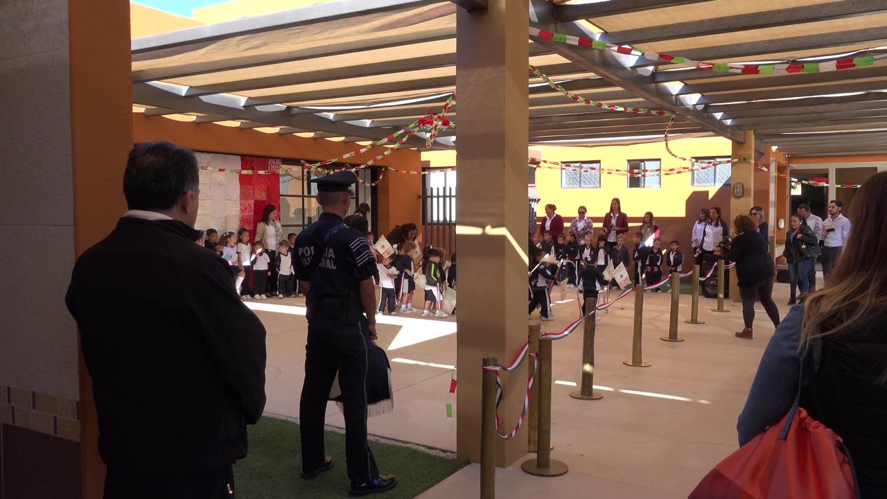 At 0:01 in San Jose del Cabo, Mexico, the courtyard view shows children along the back wall, adults clustered near the entrance, rope barriers, and festive red, white, and green hanging decorations.