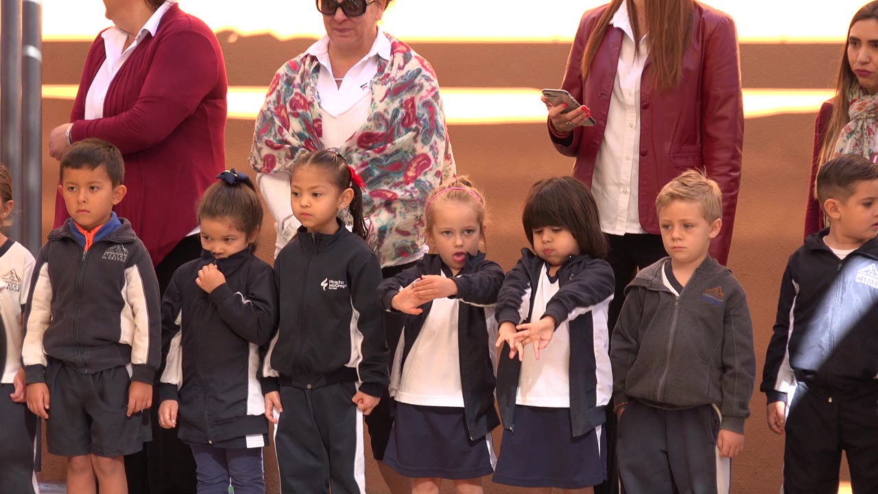 Children in recital outfits stand in front of adult supervisors.