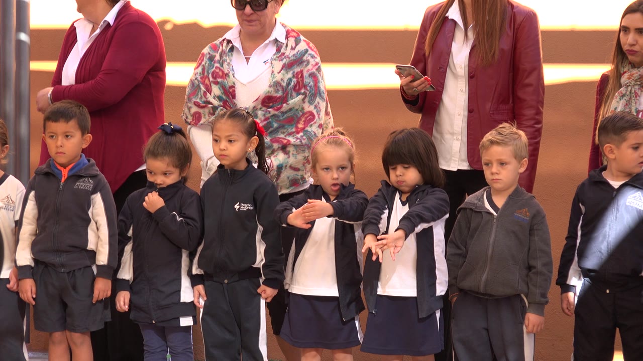 Young children in coordinated outfits wait in a line in San Jose del Cabo, Mexico, while adult supervisors stand behind them, one checking a phone.