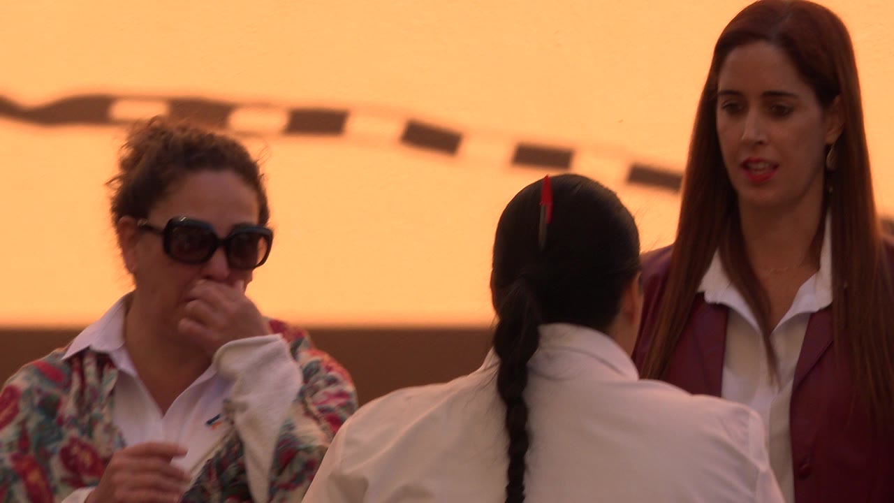 An adult in sunglasses and an adult in a maroon jacket stand beside a child with a braided ponytail in San Jose del Cabo, Mexico.