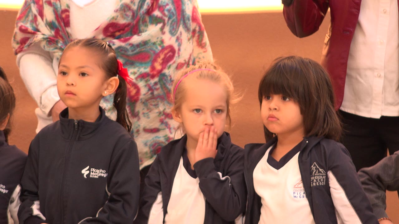 Three young girls in sportswear stand in front of adults.