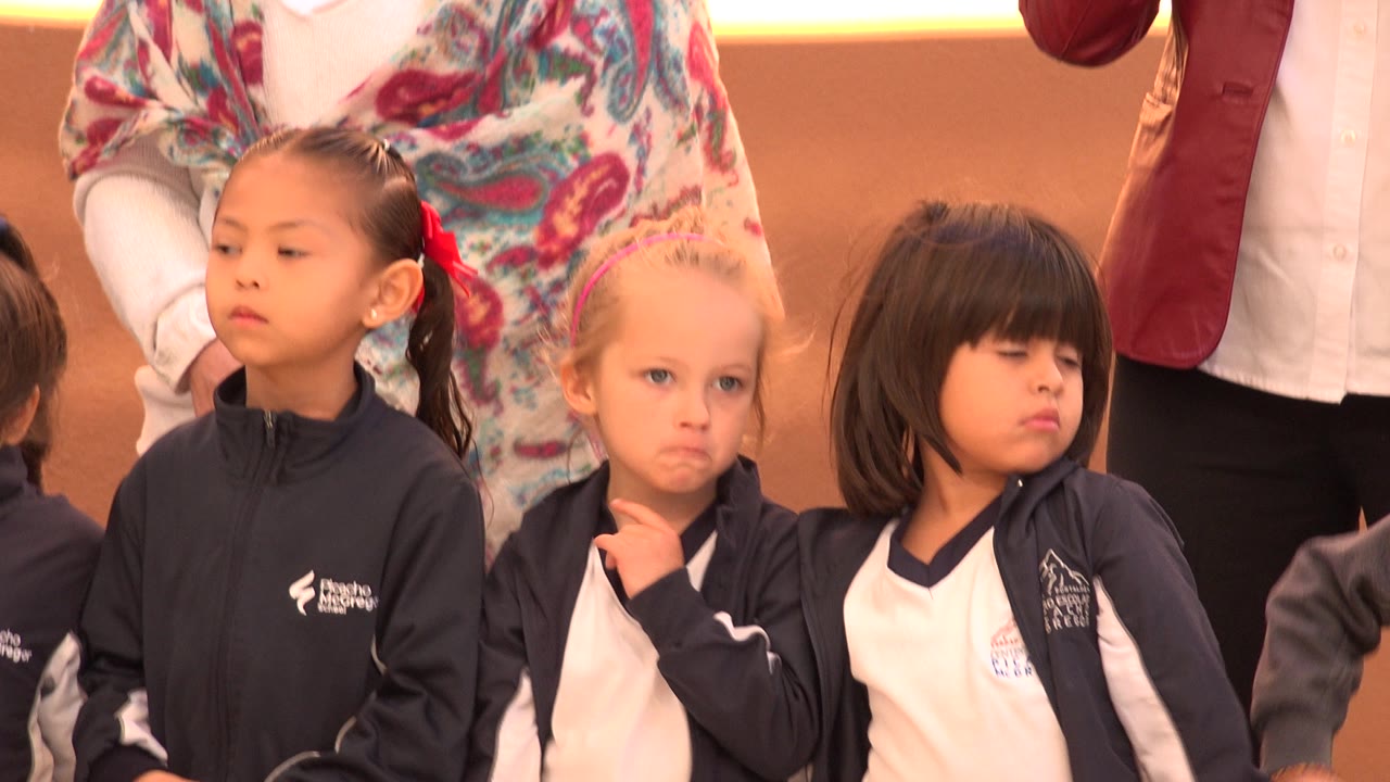 Three young girls in matching sportswear stand in a tight group in San Jose Del Cabo, Mexico, as the blond-haired girl touches her chin and the girl beside her looks away.