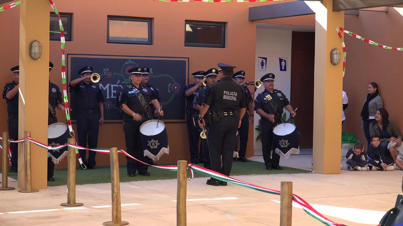 Uniformed police officers in San Jose del Cabo, Mexico, play drums and brass instruments in a decorated courtyard while children and adults watch from the side.