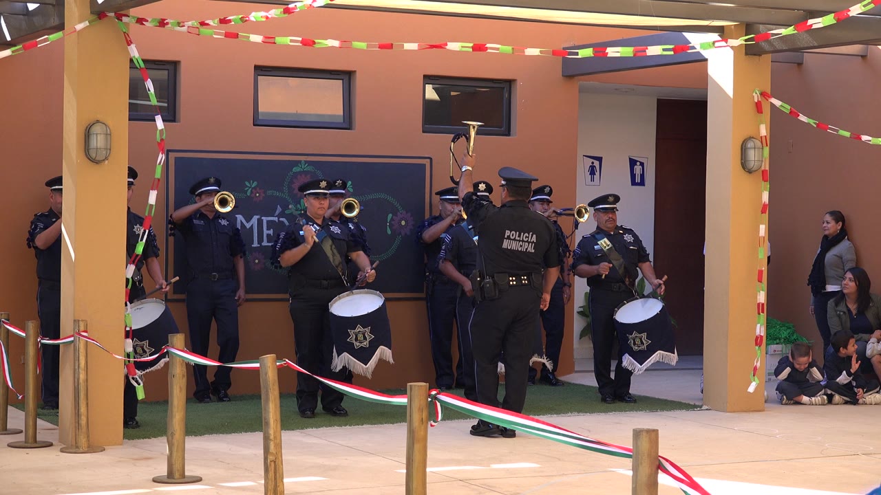 The San Jose del Cabo band remains centered as a drummer faces forward, trumpet players stand to the left, and a uniformed figure with Policia Municipal text is visible from behind.