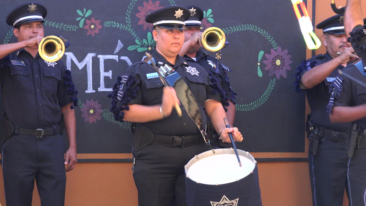 At 0:00 in San Jose Del Cabo, Mexico, a uniformed drummer stands foreground while trumpet players perform behind a chalkboard-style floral backdrop.