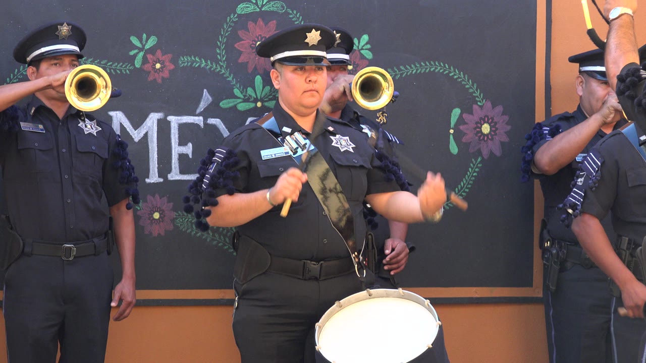 Uniformed drummer with trumpet players behind a chalkboard-style backdrop.