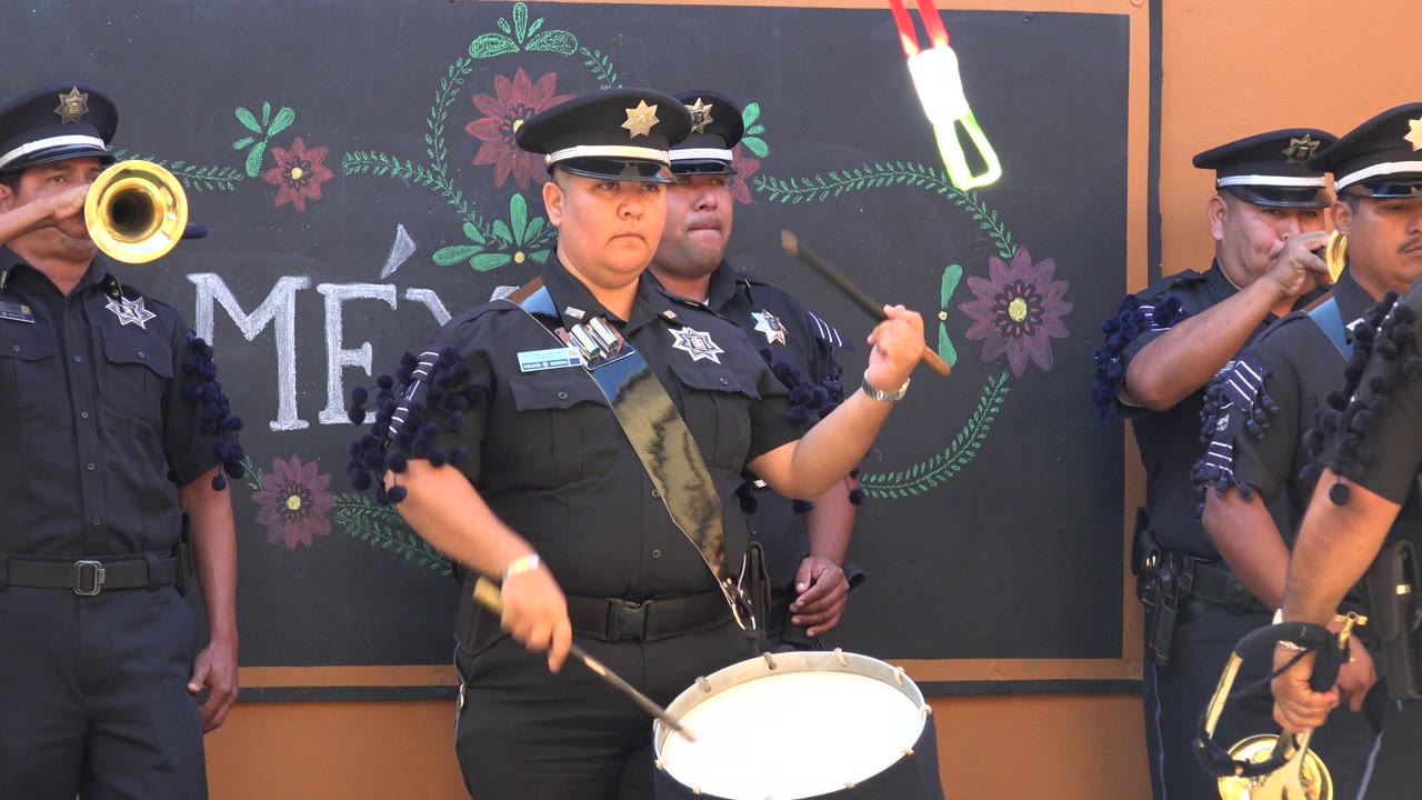 Uniformed drummer and brass players in front of a decorated backdrop.