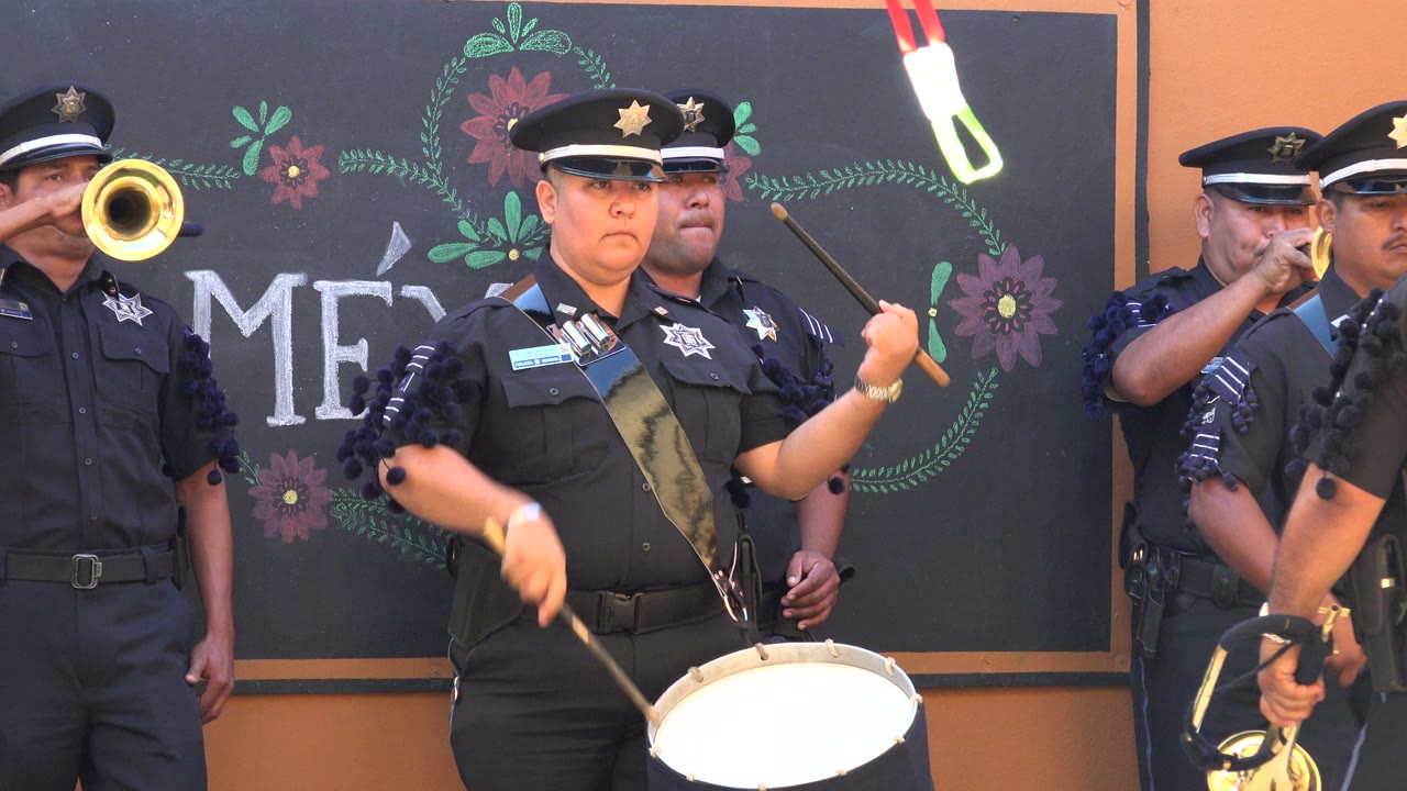 In San Jose del Cabo, Mexico, the drummer's sticks are raised over the snare as a brass player aims a horn toward the camera beside the decorated backdrop.