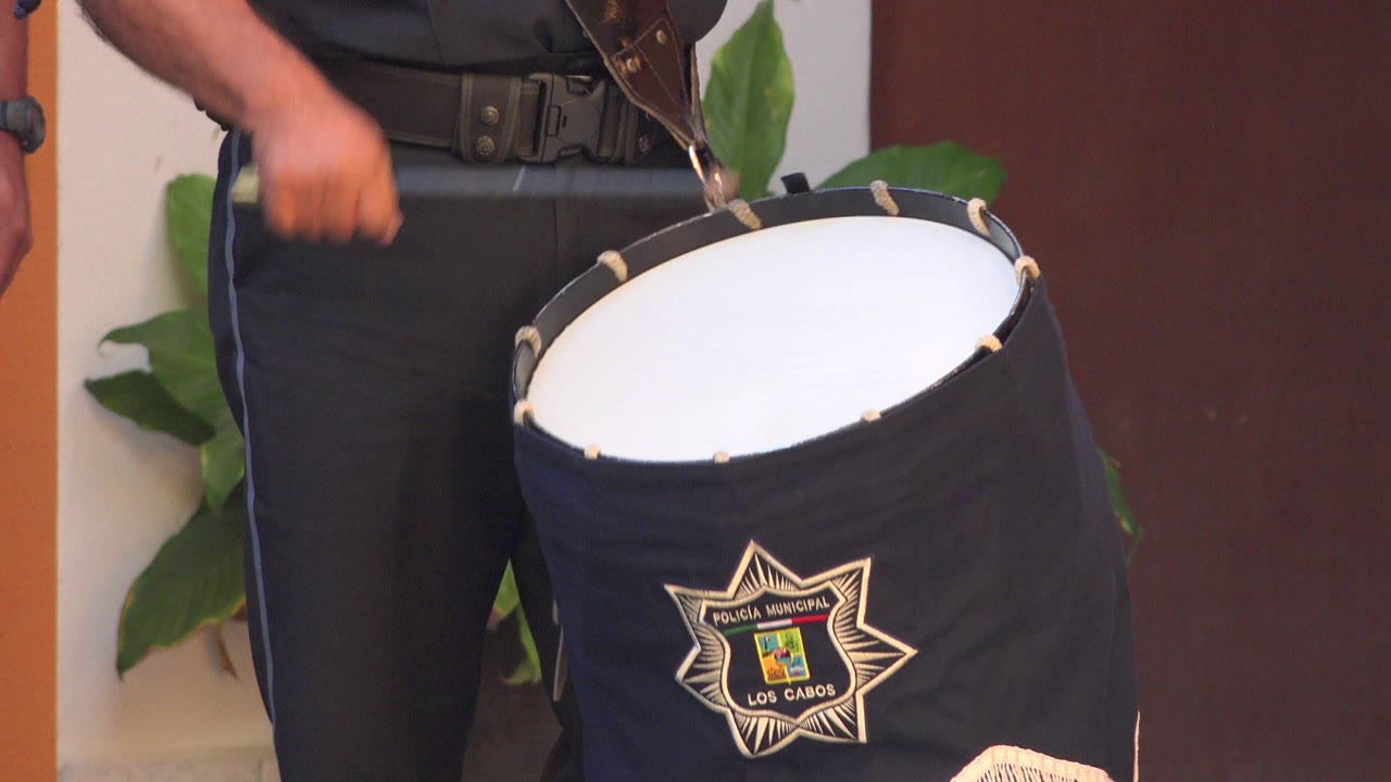 Close view in San Jose del Cabo, Mexico of a black drum with a white head beside the lower torso of a person in black pants, with green leaves and a dark red door behind.