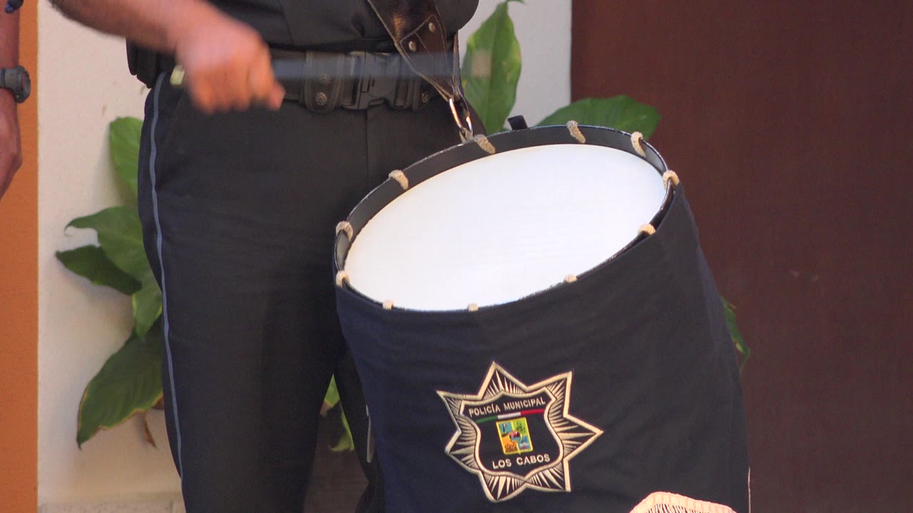 A person's arm blurs above a black and white drum in San Jose del Cabo, Mexico, with the drum's municipal-style badge visible on its dark cover.