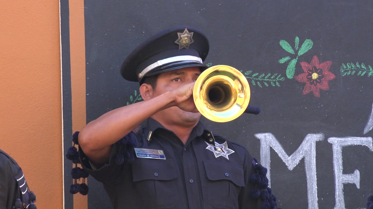 Uniformed police officer playing a trumpet in front of a chalkboard wall.
