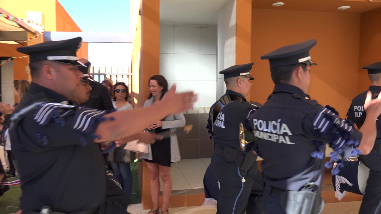 Municipal police officers march past clapping spectators outside an orange building.