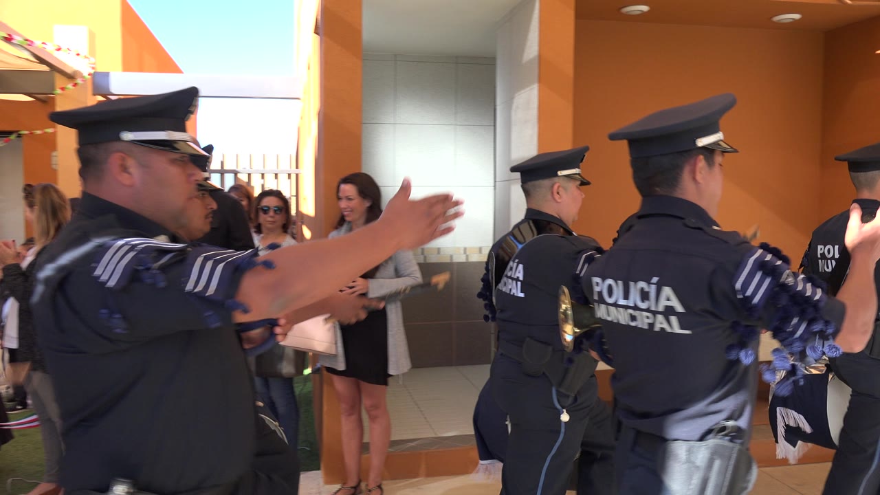 A line of San Jose del Cabo municipal police officers moves past women standing by a doorway, with one officer's arm blurred in the foreground.
